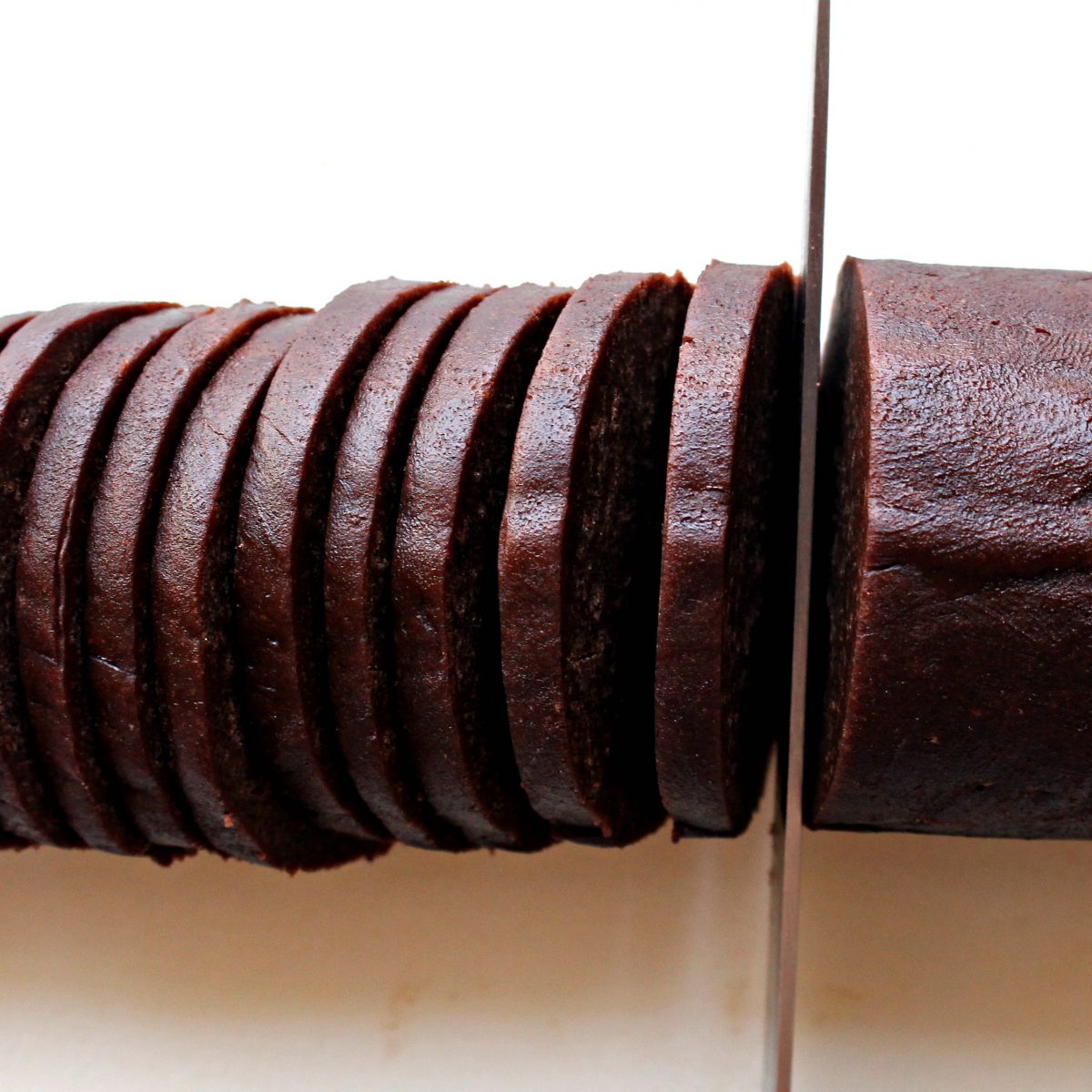 Cookie dough log being sliced into thin cookies.