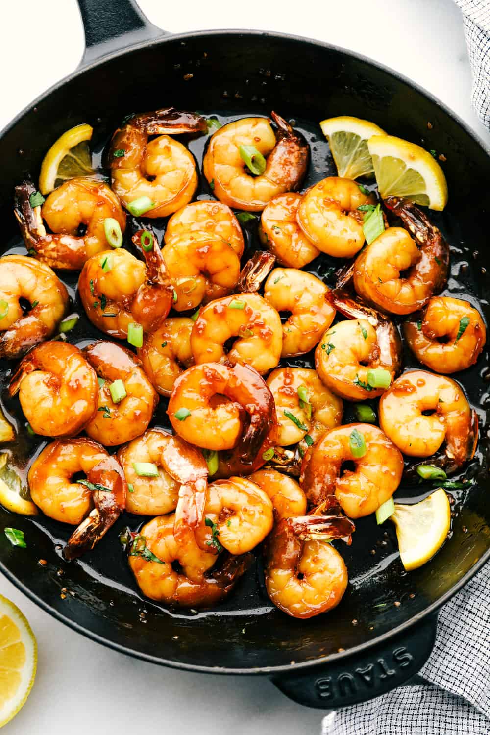 Sticky honey garlic butter shrimp cooking in a skillet garnished with lemons. 