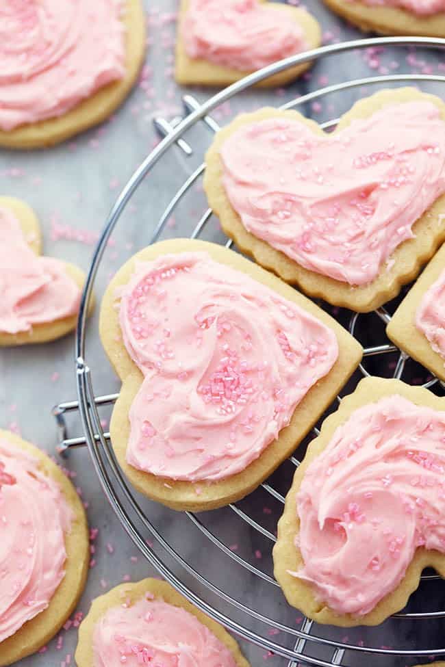 Frosted sugar cookies with sprinkles on a cooling rack.