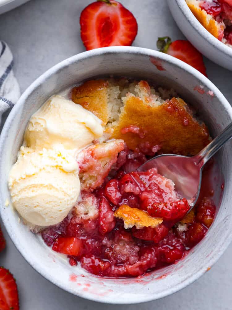 The top view of strawberry cobbler in a bowl with a spoon and some vanilla ice cream. 