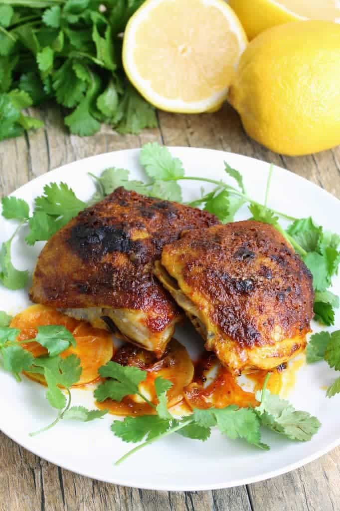 Moroccan seasoned chicken thighs on a white plate with cilantro and lemon slices.