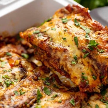 Enchiladas being pulled out of a baking dish with a spatula.