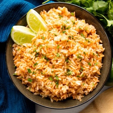 Bird's eye view of spanish rice in a black bowl topped with lime wedges.