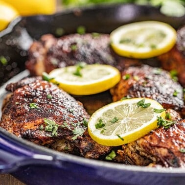 Close up view of cooked chicken thighs in a skillet with lemon slices on top