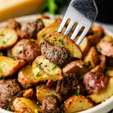 A close up view of a fork lifting a bite of steak bites and potatoes from the plate.