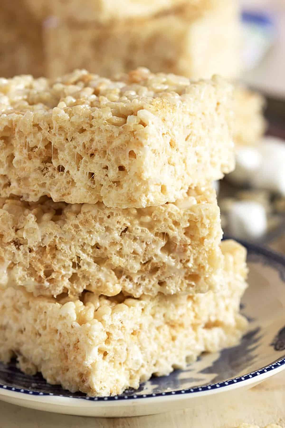 Three crispy cereal treats stacked on top on a blue and white plate.