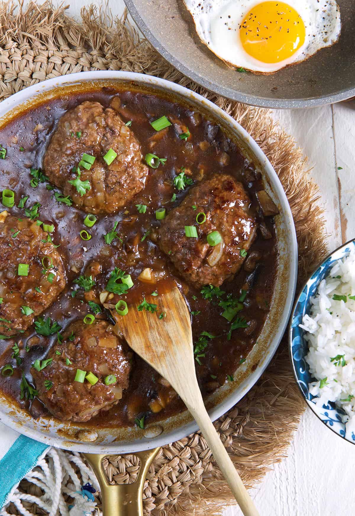 Several beef patties were cooked in gravy in a round skillet.