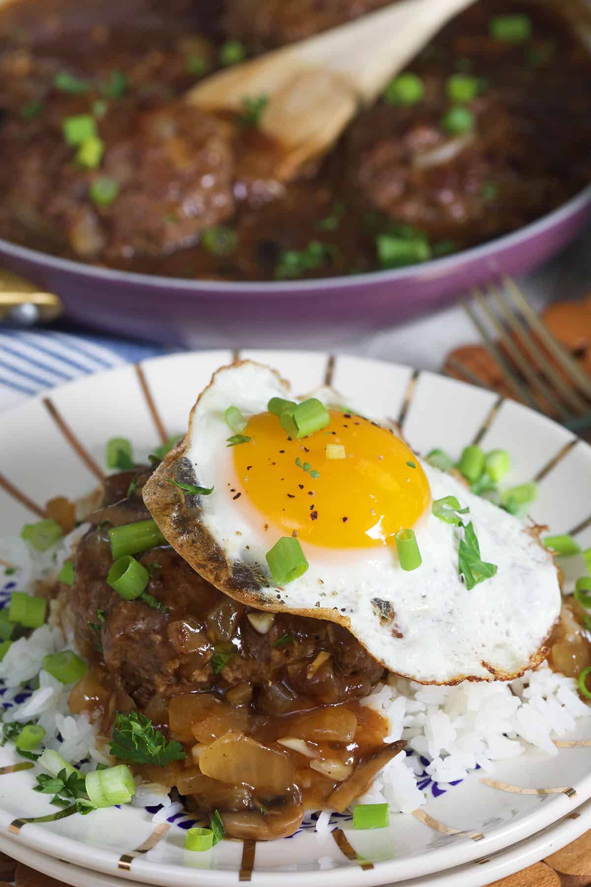 A fried egg is placed on top of a serving of rice and cooked meat with brown sauce.