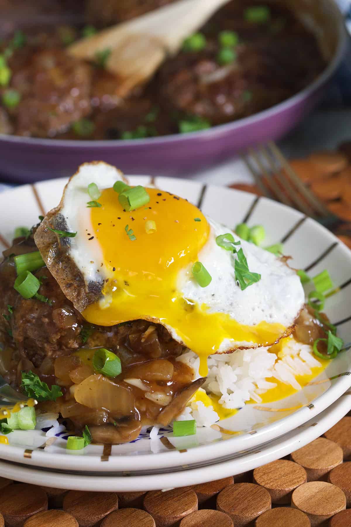 A fried egg has been cut into and the yolk is speading onto the rest of the Loco Moco. 