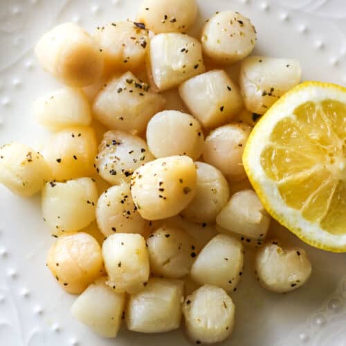 air fryer bay scallops on the white plate with half of lemon next to them