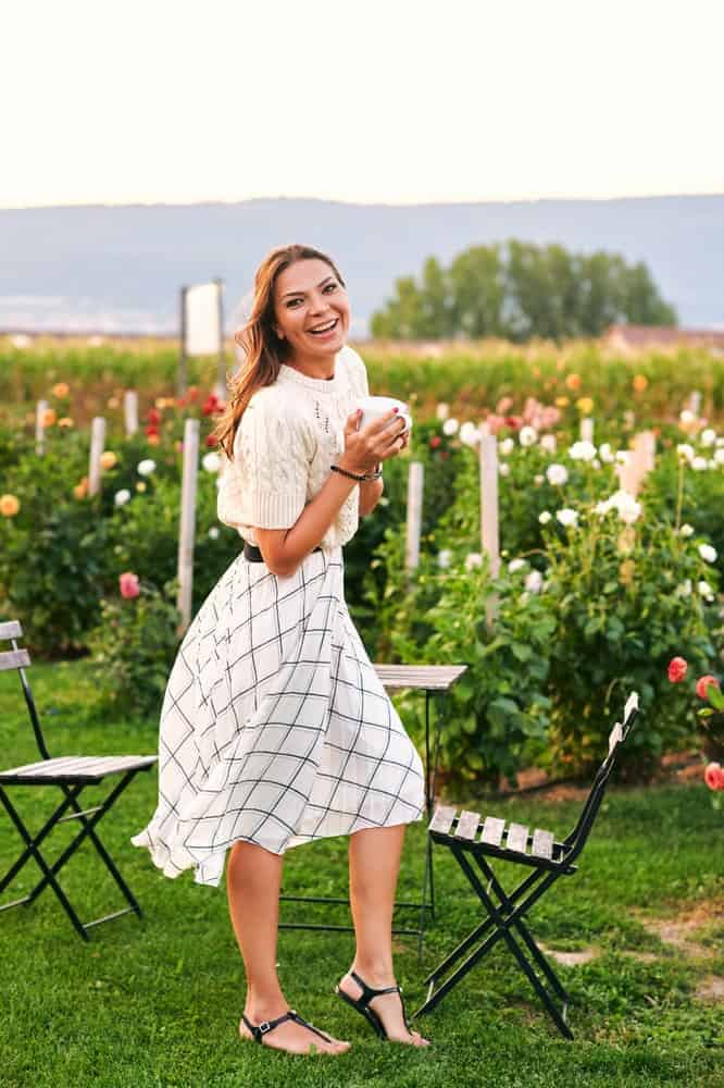 Woman in tea-length skirt holding a cup of coffee in a garden.