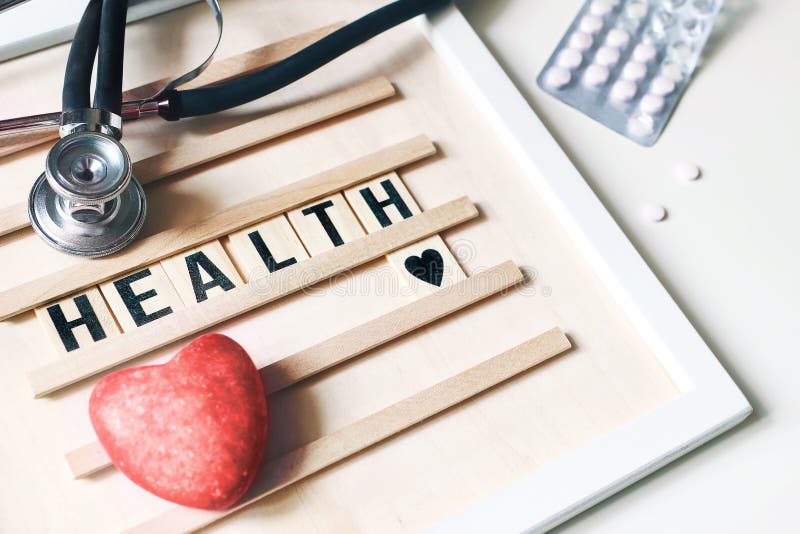 Closeup of red heart stone, stethoscope, wooden letter board and pills on white table background. Health care, medical royalty free stock image