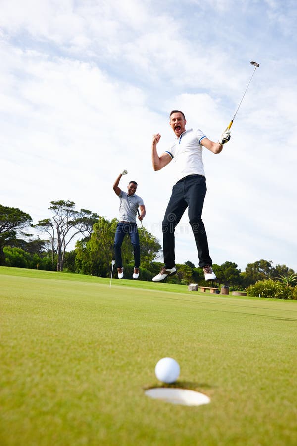 How could golf ever be boring. Low angle shot of a golf ball approaching the hole while two golfers look on. royalty free stock photography