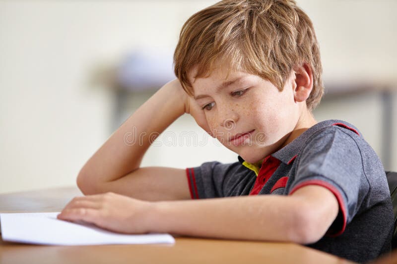 Who ever likes a test. A school boy sitting at his desk looking bored. stock photo