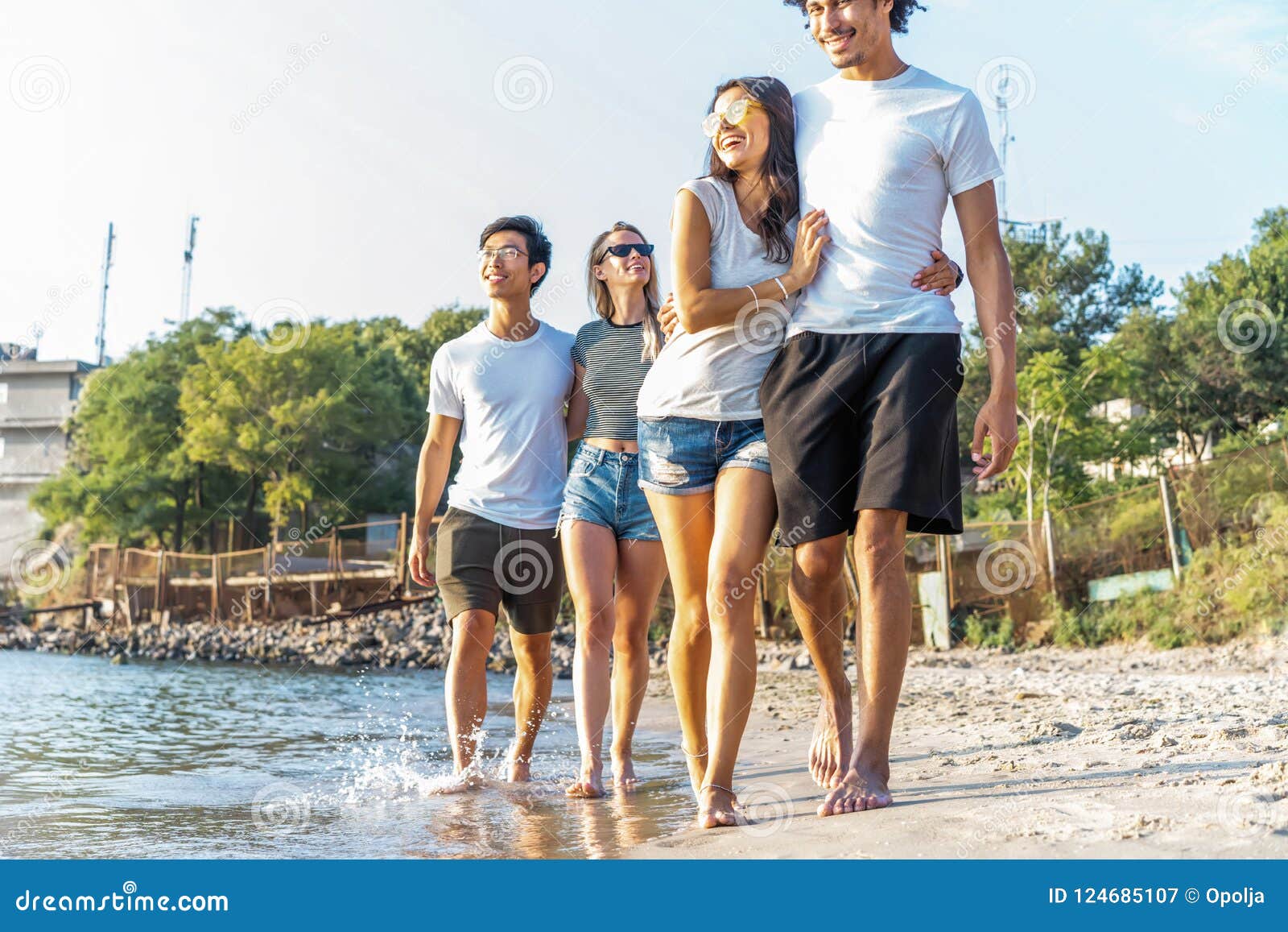 Group Of Friends Run Through Waves Together On Beach 