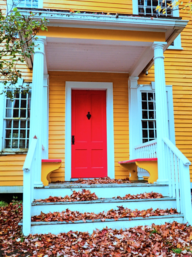 Yellow New England house and porch with red door and fall leaf covered white steps