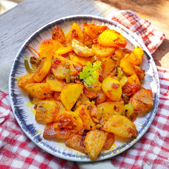 Aloo shimla mirch arranged in white plate on red white check cloth