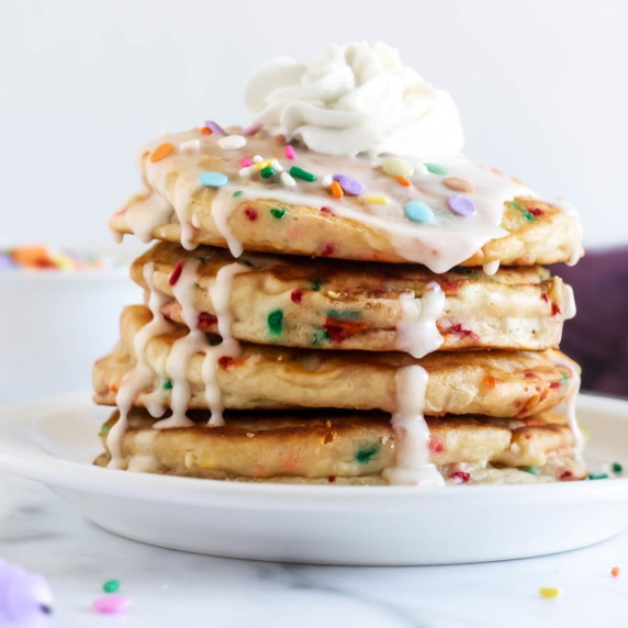 stack of funfetti pancakes topped with vanilla glaze, sprinkles, and whipped cream.