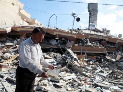 A man looks into a book he's holding as he stands beside the rubble of a building