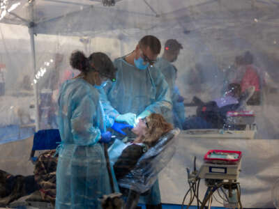 Two dentists in full ppe work on the mouth of a patient in a remote clinic