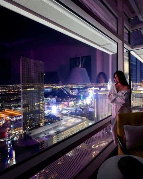 a woman standing in front of a window looking out at the city lights ...