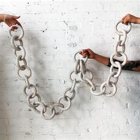 two hands holding chains in front of a white brick wall