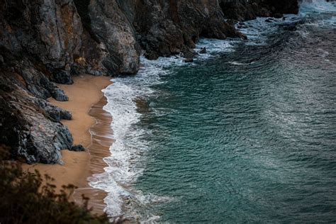 A sandy beach next to a rocky cliff photo – Free Grey Image on Unsplash