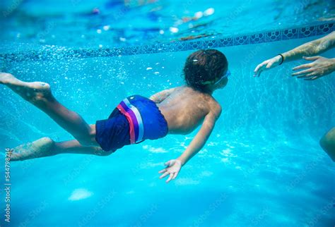 Young diverse boy swimming underwater in a swimming pool. Learning to ...