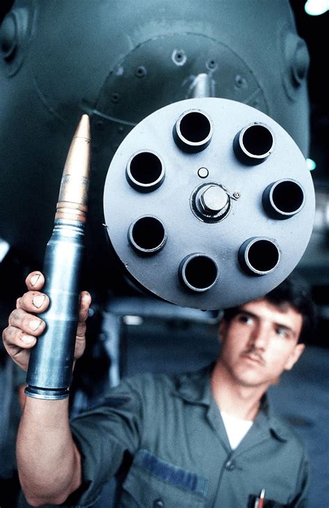 A soldier stands below a GAU-8 Gatling Gun and holds up a 30mm ...