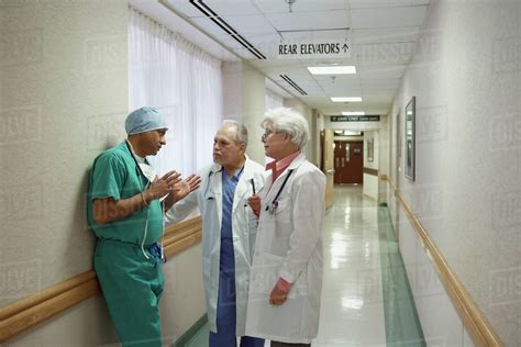 Surgeon talking to two doctors in hospital hallway - Stock Photo - Dissolve