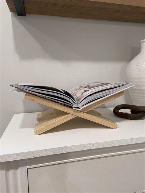 an open book sitting on top of a wooden stand next to a vase and other ...