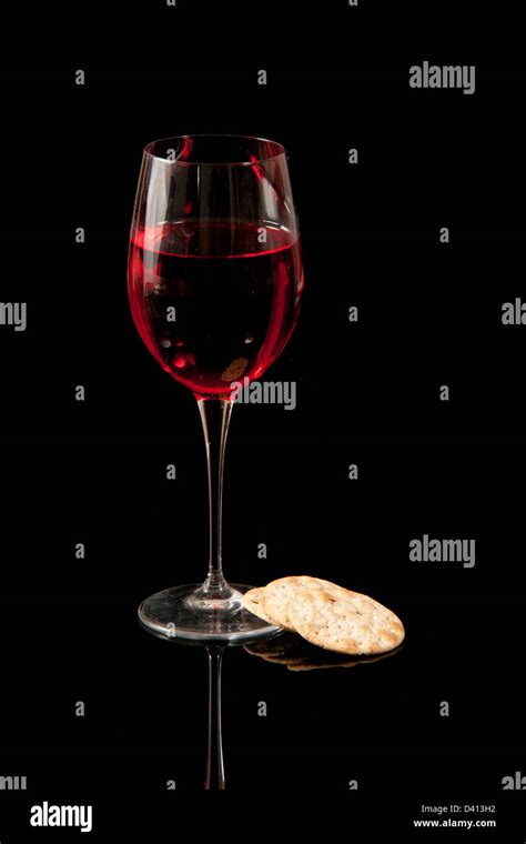 A glass of communion wine and crackers set against a black background ...