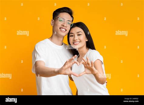 Smiling young asian couple showing heart sign with fingers Stock Photo ...