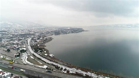 Lake, city and road in winter. Trucks travel on highway by lake in ...