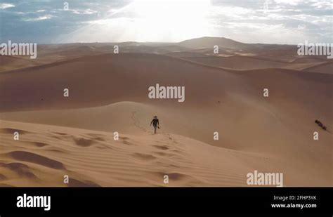 A tourist walking toward the camera, climbing a dune in Sahara desert ...