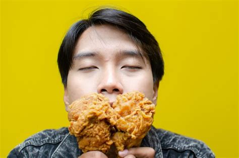 Premium Photo | Expressive asian man eats and smells fried chicken ...