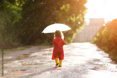 Happy child with an umbrella playing out in the rain in the summer ...