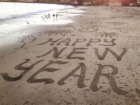 happy new year written in sand on the beach with people walking around ...