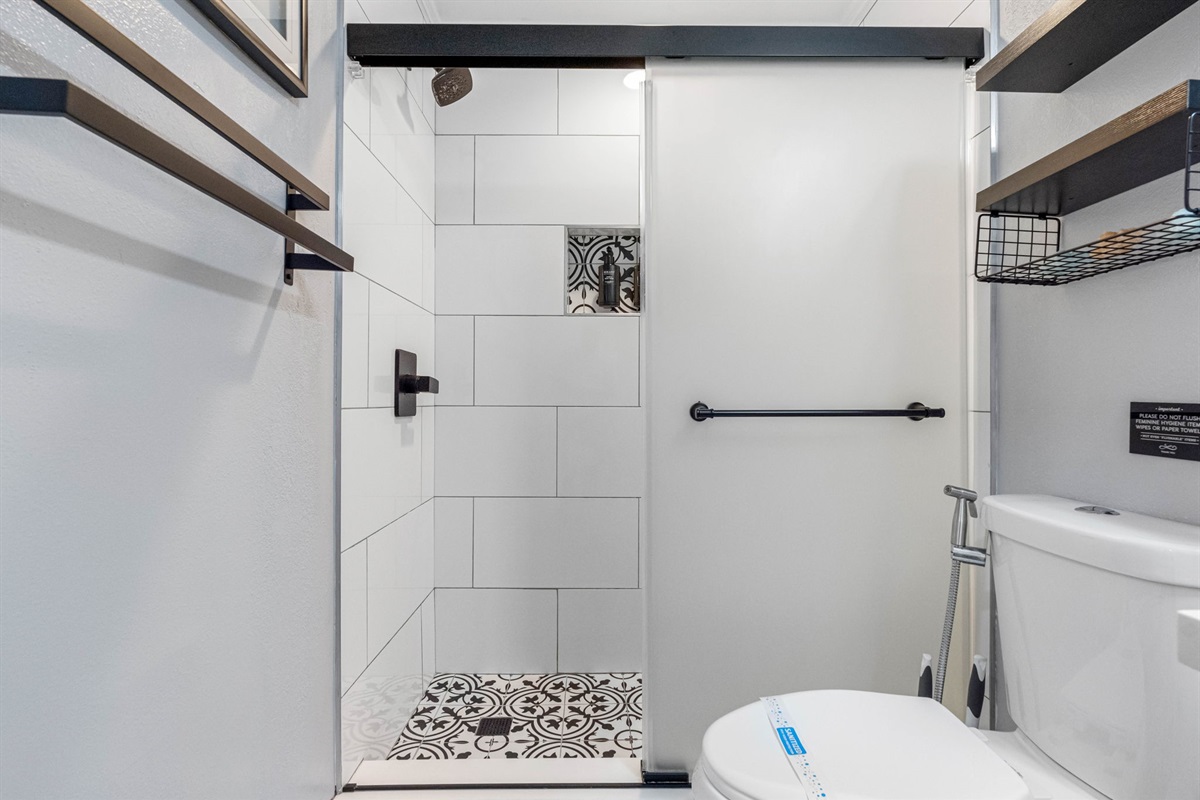 This bathroom offers a sleek, modern design with a striking black-and-white color scheme that creates a timeless and elegant atmosphere. The standout feature of this space is the walk-in shower, enclosed in frosted glass that offers both privacy and style.