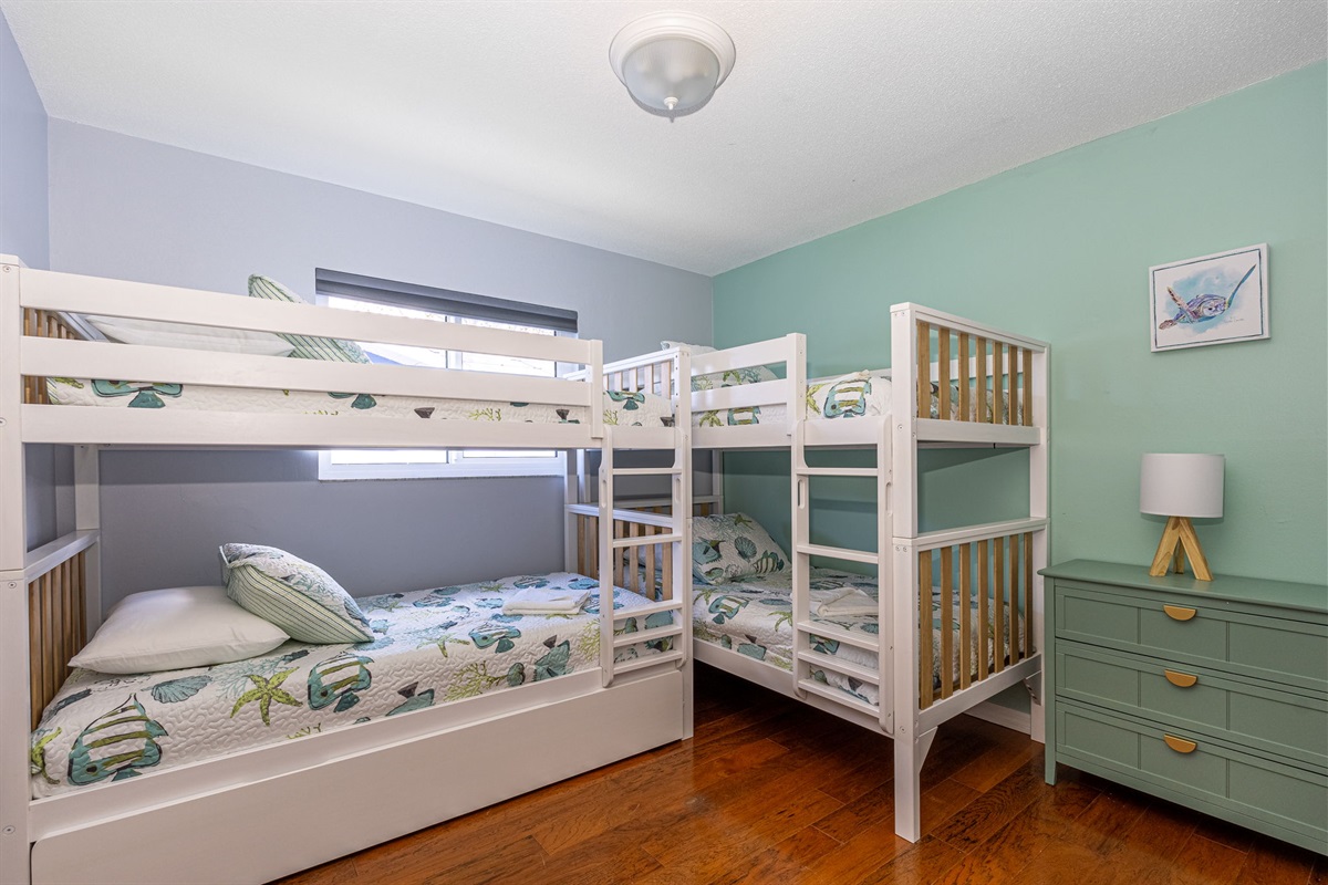 One of the standout features of this room is the beautiful aquamarine accent wall that serves as a striking backdrop for the bunk beds. The cool, tranquil hue of the wall evokes a sense of calm and relaxation.