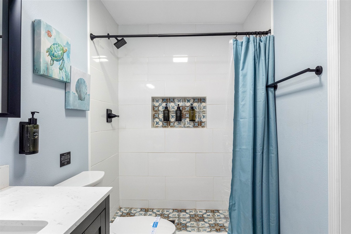 This bathroom is designed with a spacious walk-in shower, featuring a cool blue shower curtain that introduces a soothing pop of color. The soft, tranquil tones of the curtain contrast beautifully with the rest of the room, enhancing the serene ambiance.