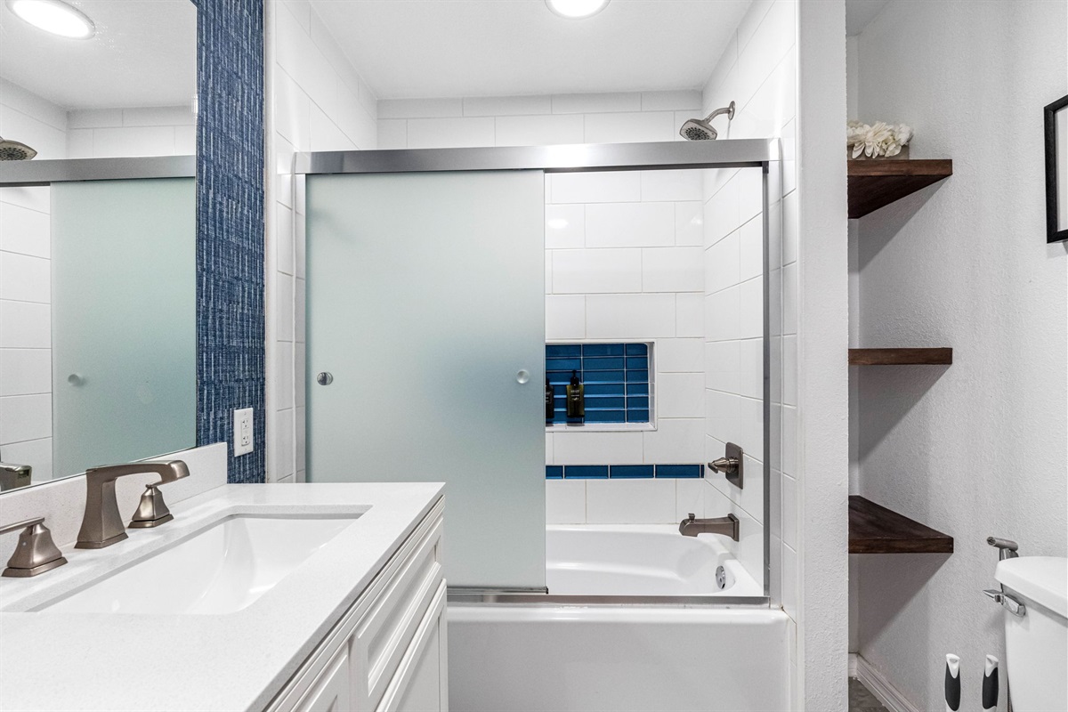 The bathroom also includes a tub-and-shower combination, enclosed in frosted glass providing both privacy and a sleek, modern look.