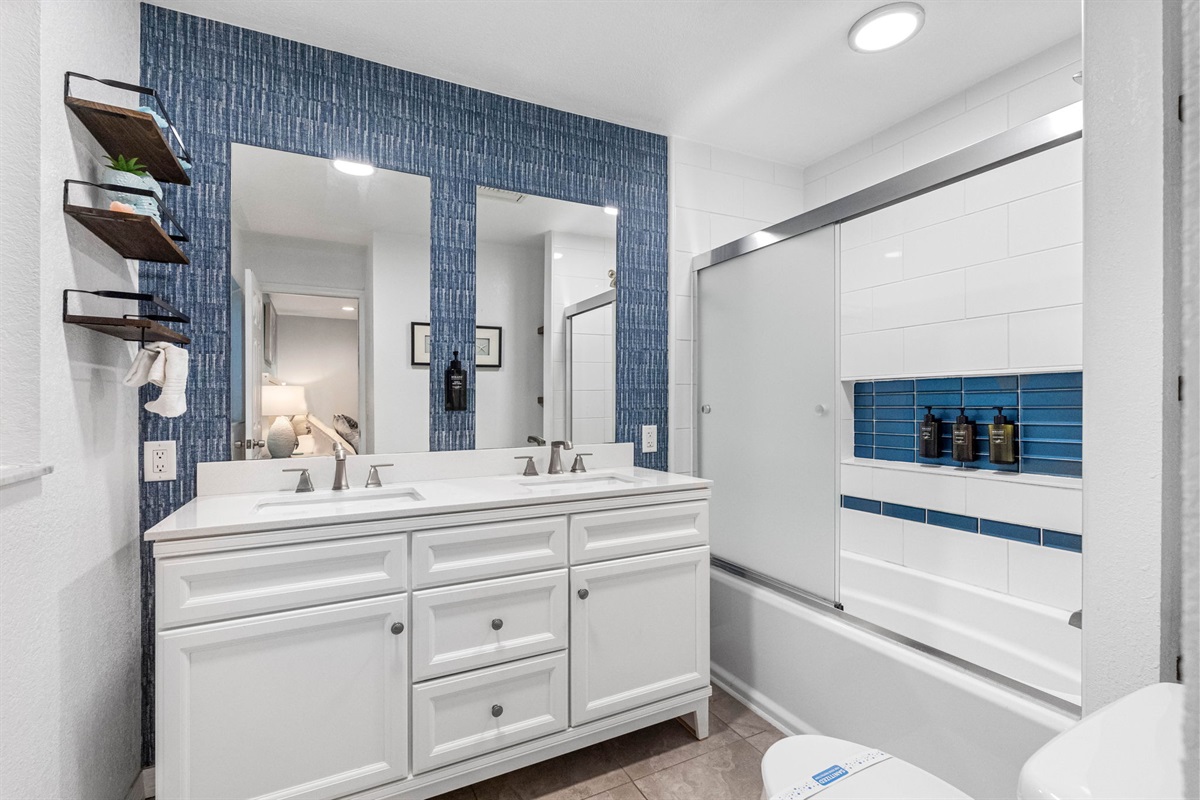 This beautiful bathroom offers a luxurious and functional design, featuring a spacious his-and-hers sink setup that are set within a stunning vanity that is complemented by a gorgeous blue backsplash.