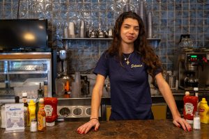 19-year-old Tess Frangias, co-owner of Hyde Park's Greek diner Salonica, poses behind the restaurant counter. 