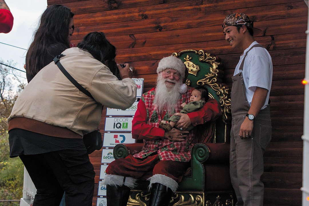 A father and baby pose with Santa for a photographer during Hometown Holidays, Dec. 14, 2024, at San Marcos Plaza Park.