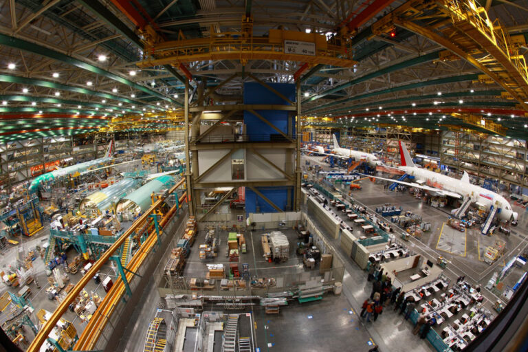 The bustling interior of a large aircraft manufacturing facility offers a unique glimpse into Seattle's vibrant industrial side, with airplanes in various assembly stages. Amidst machinery and scaffolding, workers thrive under bright lighting—an intriguing addition to the list of things to do in Seattle.