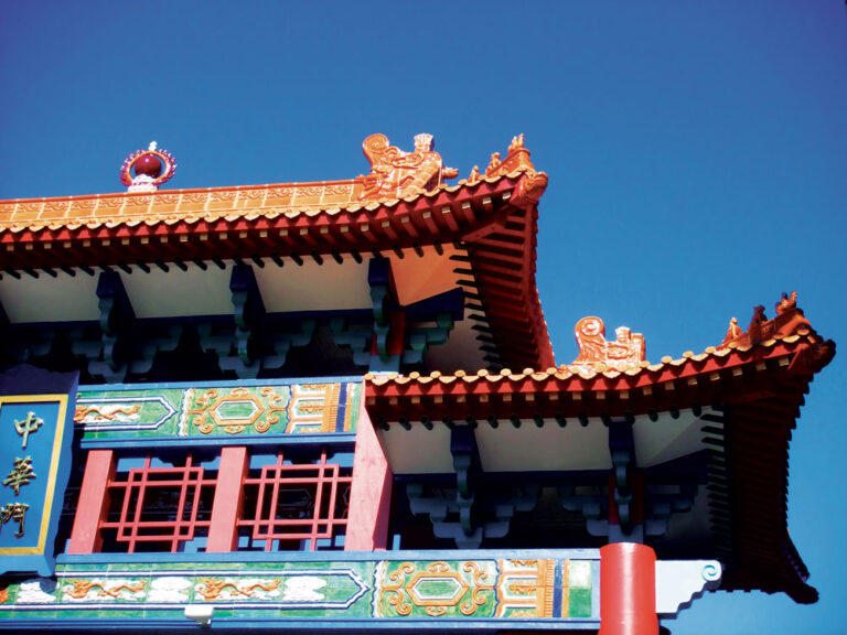 A vibrant Chinese temple roof with intricate designs and red, green, and blue details stands proudly against Seattle's clear blue sky. The architecture features ornate carvings and traditional Chinese motifs, showcasing the cultural artistry among the must-see things to do in Seattle.