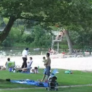 Families enjoying Reservoir Beach with a sandy area, playground, and lifeguard tower visible in the background.