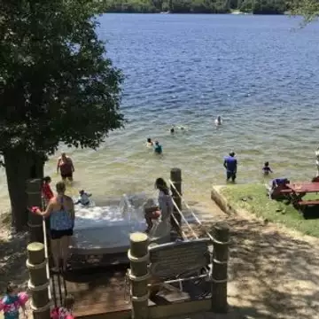 Families enjoying a sunny day at Breezy Picnic Grounds with swimmers in the lake and picnic areas nearby.