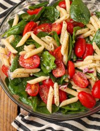 spinach tomato pasta in bowl with black and white towel